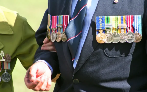 Close-up of Australian Army Veteran soldier holding the arm of a female World War widow wearing medals during ANZAC Day service